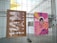 Two posters are hanging on a metal wire fence, one on the left with Japanese characters on a brown background, featuring a design that appears folded. The poster on the right has a pink background with an illustrated face and colorful abstract patterns, including text in vibrant colors.