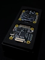 Close-up view of an electronic circuit board encased in a black rectangular container. The visible components include microchips, a USB port, and other small electronic parts. Yellow circular fixtures can be seen securing parts of the device.