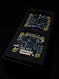 Close-up view of an electronic circuit board encased in a black rectangular container. The visible components include microchips, a USB port, and other small electronic parts. Yellow circular fixtures can be seen securing parts of the device.