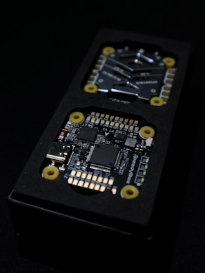 Close-up view of an electronic circuit board encased in a black rectangular container. The visible components include microchips, a USB port, and other small electronic parts. Yellow circular fixtures can be seen securing parts of the device.