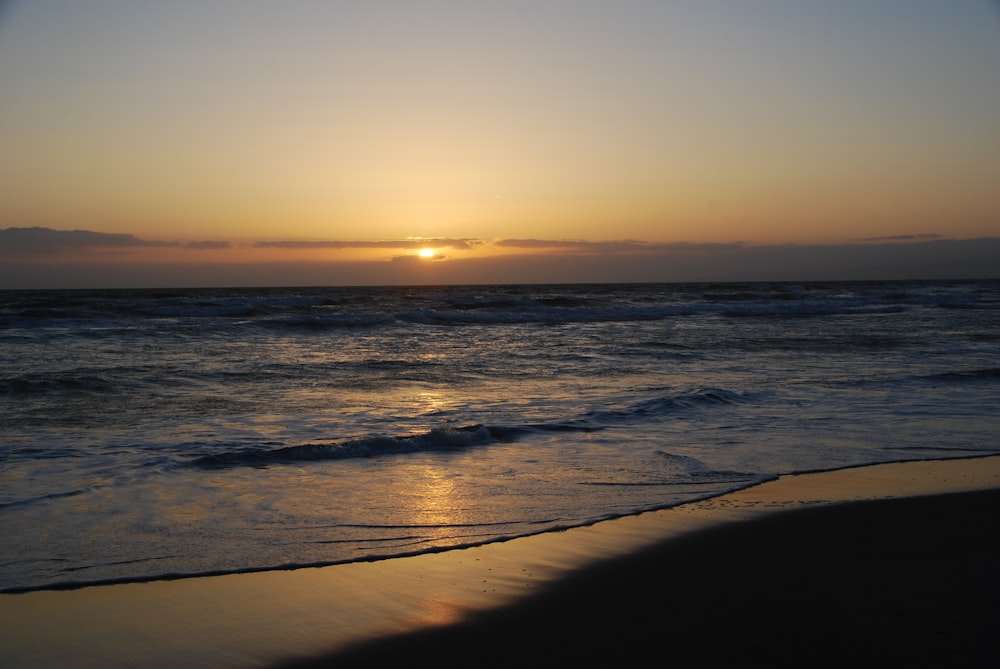 a beach with waves and the sun setting