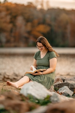 a woman sitting on a rock reading a book