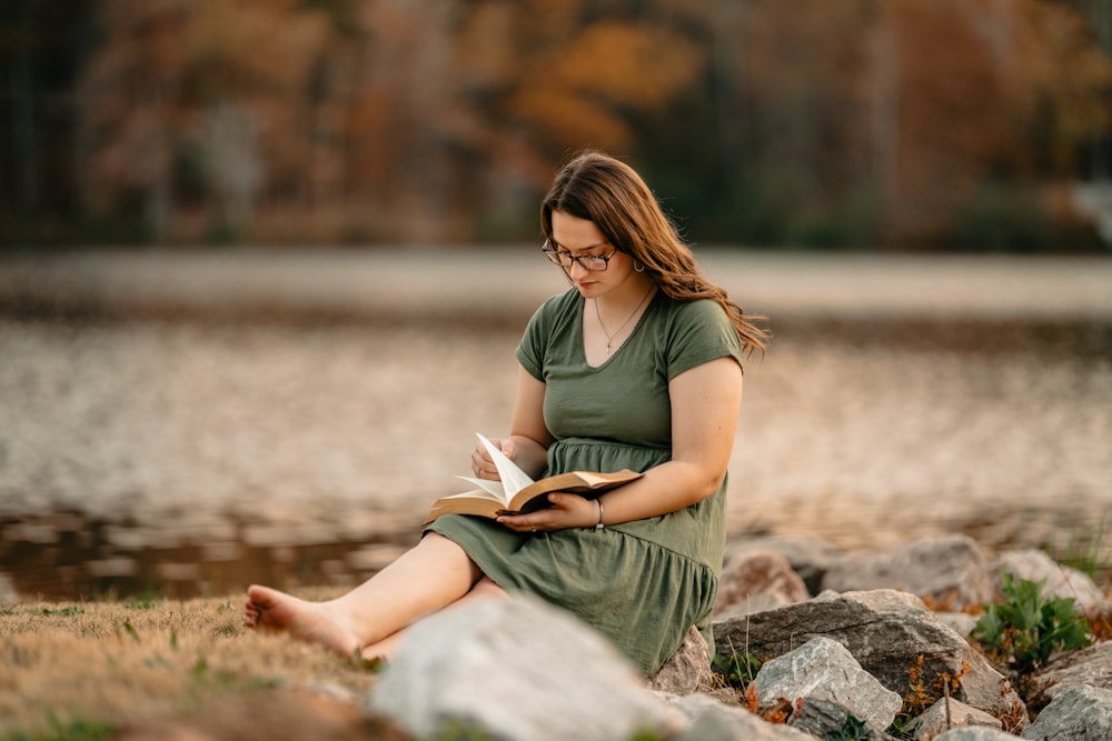 a woman sitting on a rock reading a book