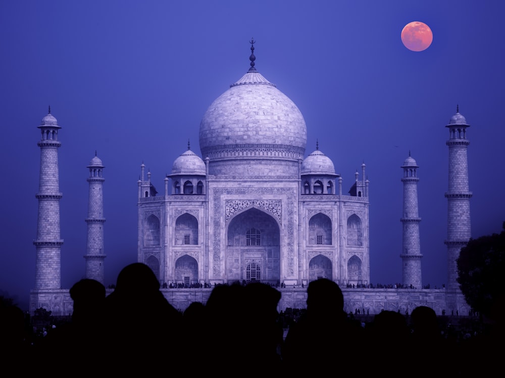 un gran edificio blanco con un techo abovedado y torres con el Taj Mahal al fondo