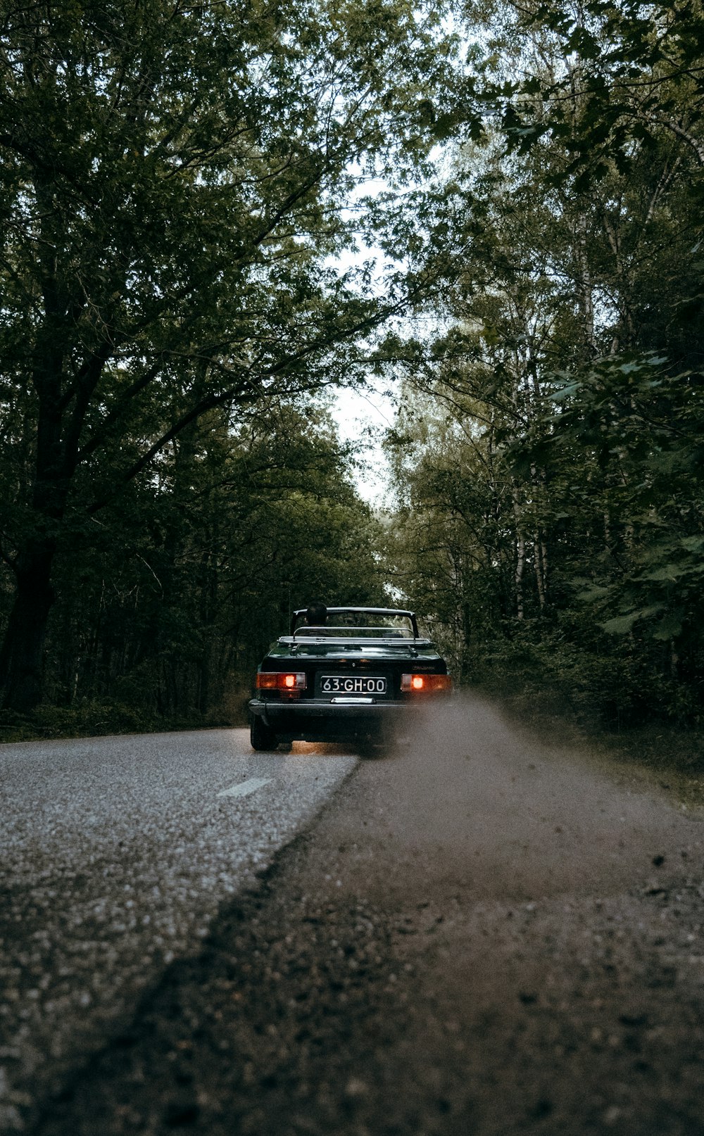 a black car parked on a road surrounded by trees