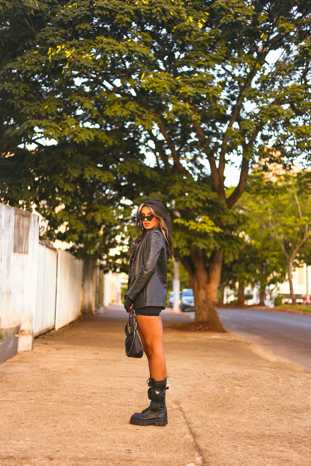 a person in a black coat and boots standing on a sidewalk