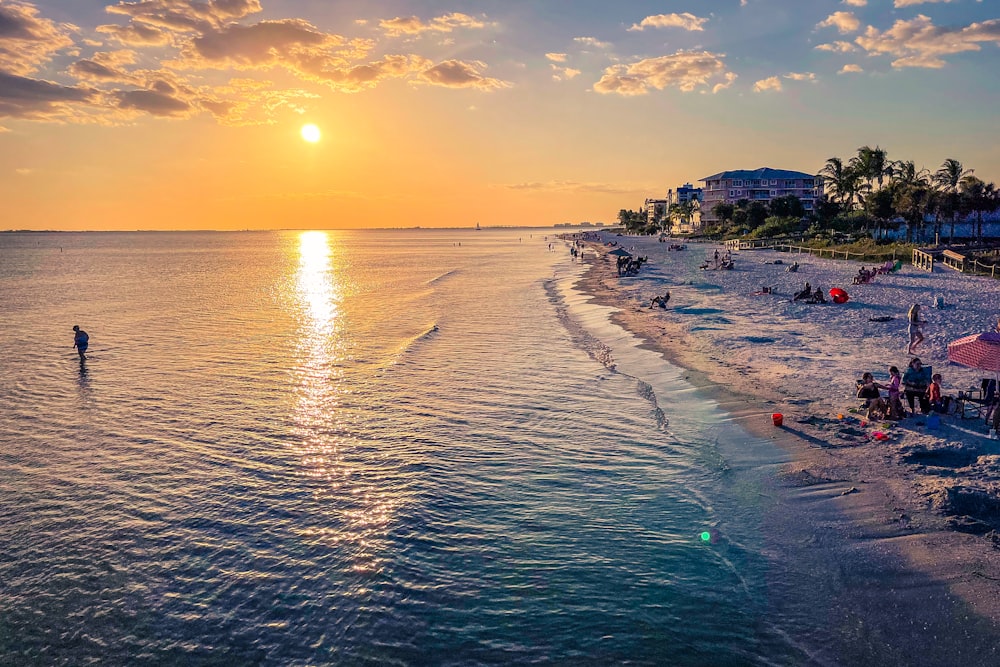 a beach with people and a body of water with a sunset