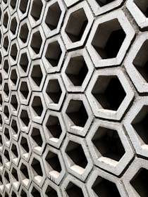 A hexagonal pattern of concrete blocks arranged in a grid, creating a uniform and structured appearance. The blocks have hollow centers and shadowed interiors, giving a sense of depth and dimension.
