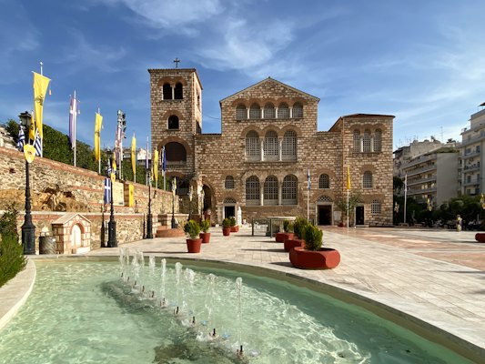 A large building with a pool in front of it with Hagios Demetrios in the background — Thessaloniki, Greece