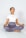 A person is meditating cross-legged on a yoga mat, wearing a white t-shirt and grey leggings, with eyes closed and in a calm posture.