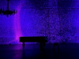 Dark studio room with a grand piano illuminated by soft blue lighting.