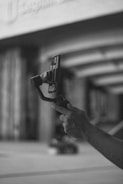A hand holding a smartphone mounted on a stabilizing gimbal in an urban environment. The image is in black and white, focusing on the technological gadget.