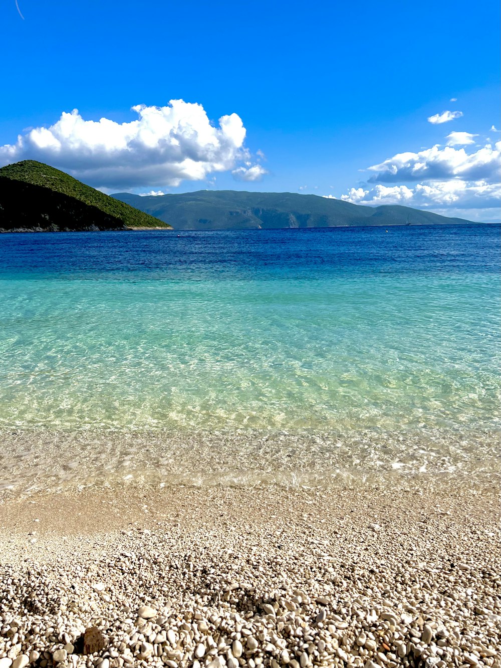 a rocky beach with a body of water and mountains in the background