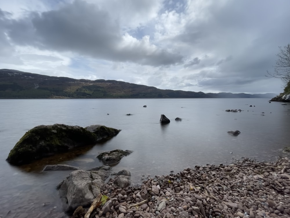 a rocky beach with a body of water and mountains in the background