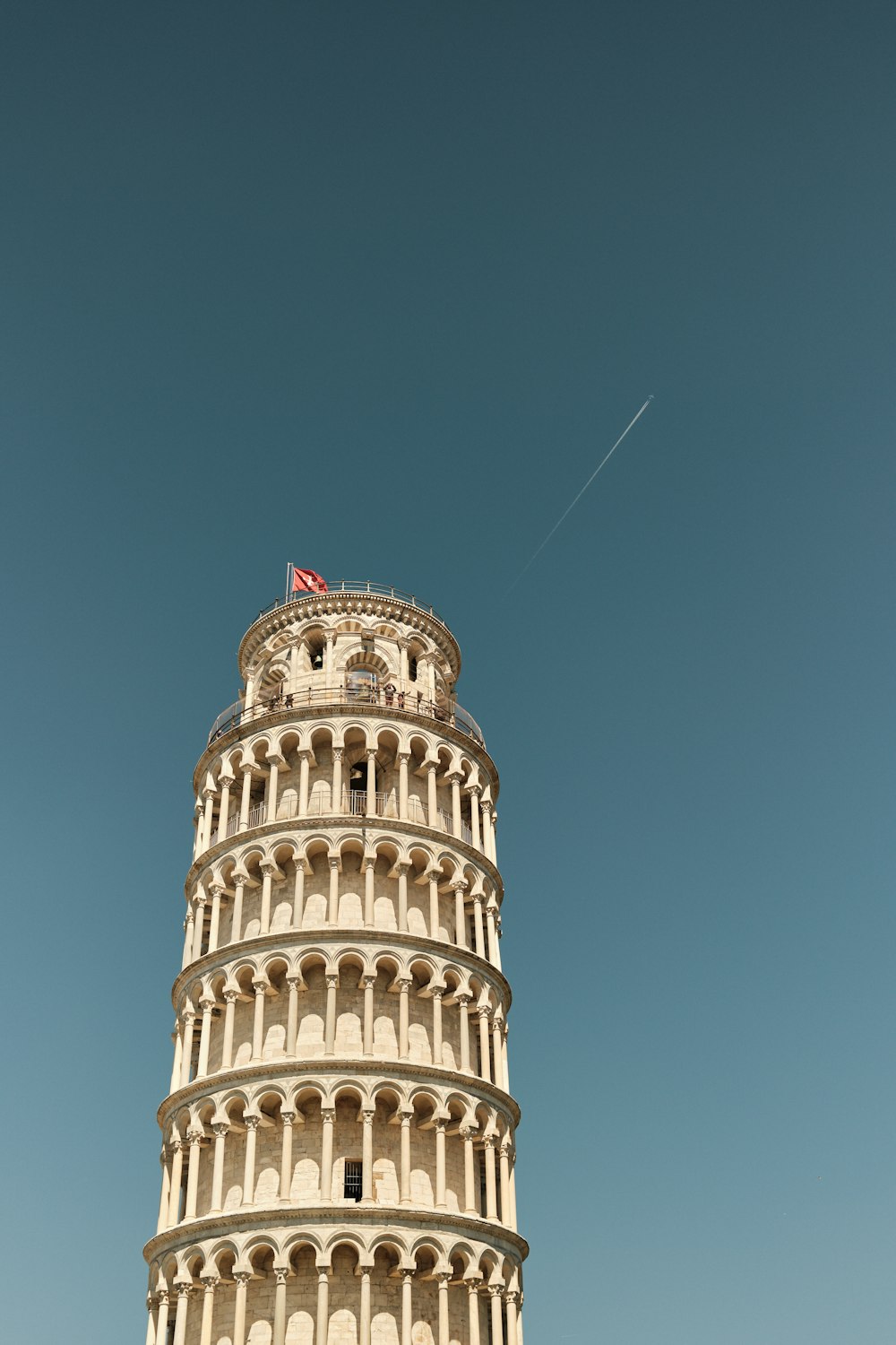 un'alta torre con una bandiera in cima con la Torre Pendente di Pisa sullo sfondo