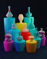 A set of vibrant, colorful vases of various shapes and patterns arranged on cylindrical pedestals of different heights. The vases have bold stripes and swirling patterns, and the pedestals are in shades of blue, yellow, pink, and red, set against a dark background.