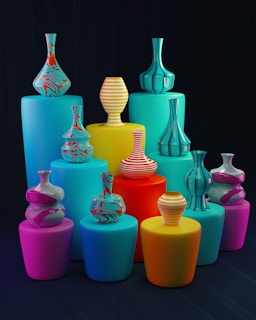 A set of vibrant, colorful vases of various shapes and patterns arranged on cylindrical pedestals of different heights. The vases have bold stripes and swirling patterns, and the pedestals are in shades of blue, yellow, pink, and red, set against a dark background.