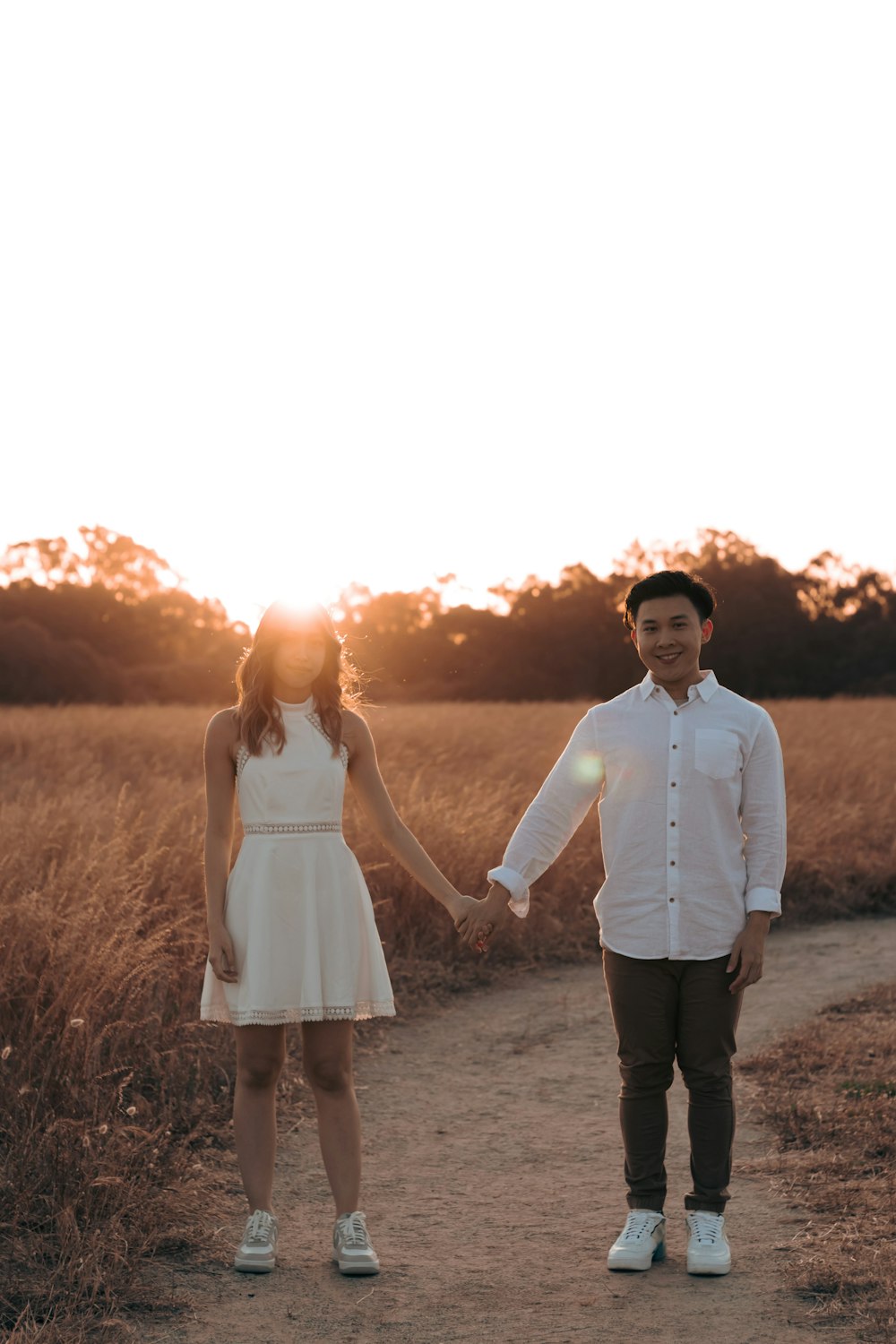 a man and woman walking on a dirt road with a sunset in the background