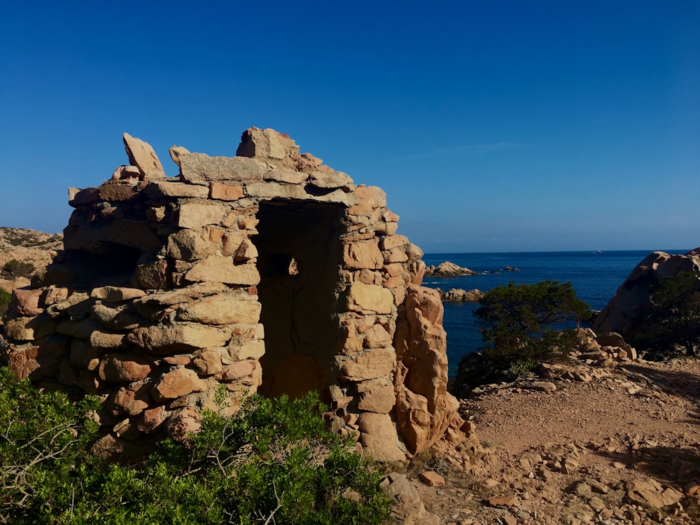 a stone structure with a hole in it with a body of water in the background