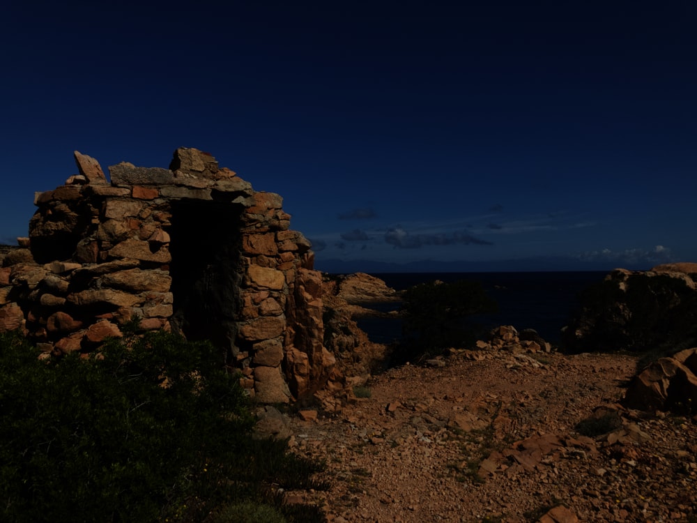 a stone structure with a hole in it with a body of water in the background