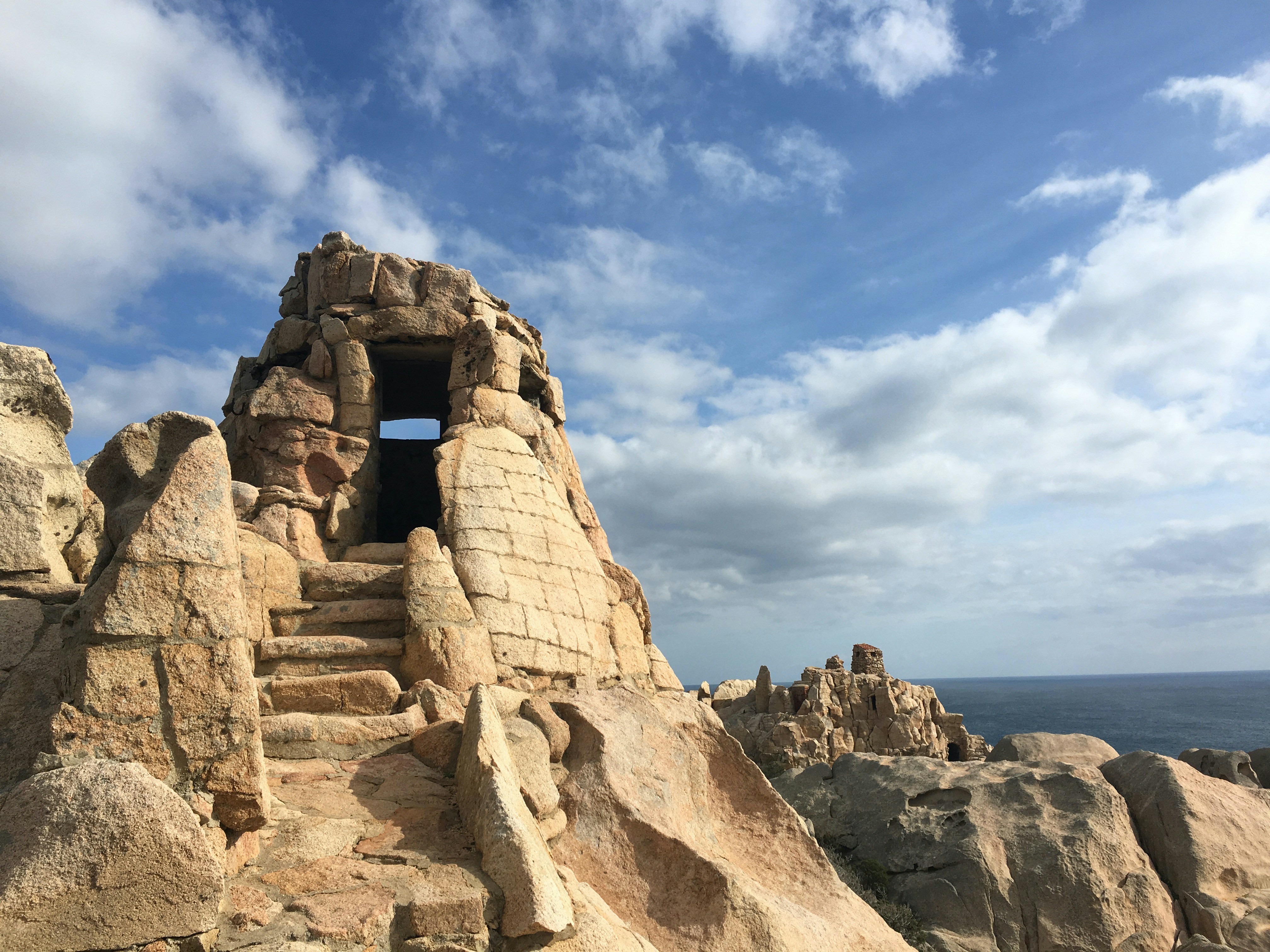 a stone building on a cliff, Walking into "The National Park of the Maddalena Archipelago" In Caprera island if you follow the footpath # 11, after 35 minutes of walking, you reach the old fortification called "Antonio CANDEO". Was built in 1928 as a medium battery to defend northeastern Caprera from ships. Simply amazing !