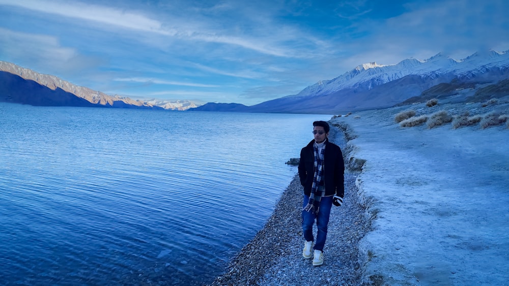 a man standing on a snowy path by a body of water