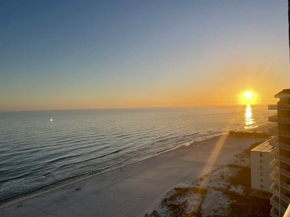 a beach with a building and the sun setting