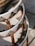 A close-up view of intricately woven rattan furniture with a geometric pattern. The craftsmanship features a combination of natural brown and white fibers, enhanced by sunlight. The image captures the texture and design of the layered wicker material.