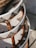 A close-up view of intricately woven rattan furniture with a geometric pattern. The craftsmanship features a combination of natural brown and white fibers, enhanced by sunlight. The image captures the texture and design of the layered wicker material.