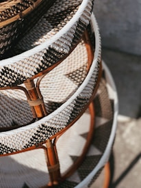 A close-up view of intricately woven rattan furniture with a geometric pattern. The craftsmanship features a combination of natural brown and white fibers, enhanced by sunlight. The image captures the texture and design of the layered wicker material.