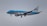 A KLM Cityhopper airplane is captured in flight against a cloudy gray sky. The plane features a blue and white color scheme, prominently displaying the KLM logo on the tail and the fuselage.