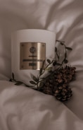 A softly glowing candle with a crescent moon design on the label, surrounded by dried flowers.