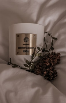 A softly glowing candle with a crescent moon design on the label, surrounded by dried flowers.