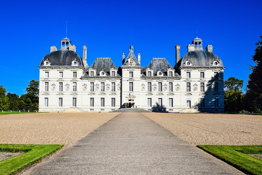 un grand bâtiment blanc avec une route devant lui avec le château de Cheverny en arrière-plan