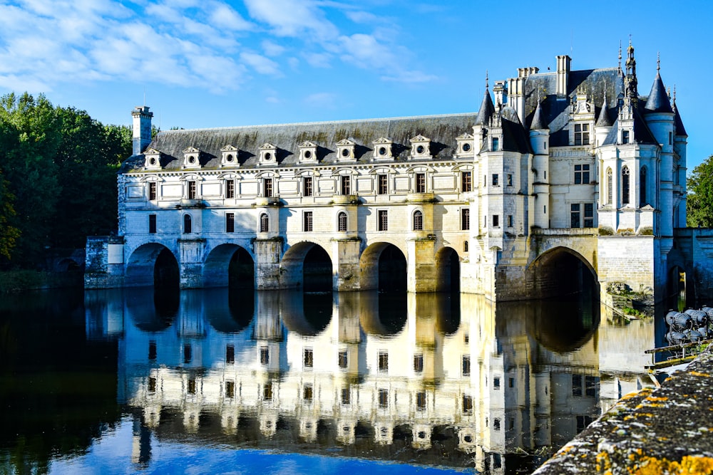 un grand bâtiment blanc avec le Château de Chenonceau sur un plan d’eau