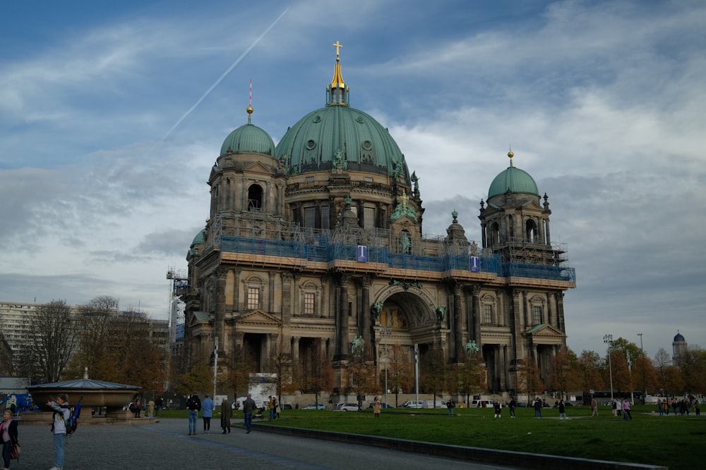a large ornate building with a green lawn and people walking around with Berlin Cathedral in the background