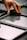 A hand is placing or adjusting a glass panel within a black metal grid structure on a gray, textured surface. The reflective quality of the glass shows faint reflections.