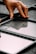 A hand is placing or adjusting a glass panel within a black metal grid structure on a gray, textured surface. The reflective quality of the glass shows faint reflections.