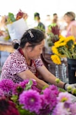 Artisan arranging a bouquet of local Tenancingo flowers in a market stall.