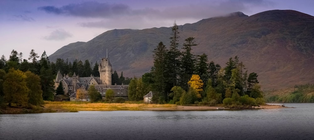 a castle on a hill by a lake with trees and mountains in the background