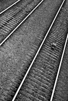 Railway tracks extend diagonally across the image, comprised of evenly spaced metal rails and wooden sleepers. The ground is covered with small, uniformly sized gravel stones. A solitary object, possibly a piece of debris, is visible on one of the tracks.