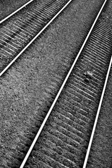 Railway tracks extend diagonally across the image, comprised of evenly spaced metal rails and wooden sleepers. The ground is covered with small, uniformly sized gravel stones. A solitary object, possibly a piece of debris, is visible on one of the tracks.