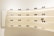 A variety of sunglasses are displayed on curved, backlit shelves in a modern showroom. The shelves are mounted on a light-colored wall, creating a clean and minimalist aesthetic. Different styles and colors of sunglasses are neatly arranged, with some featuring labels or small display signs.