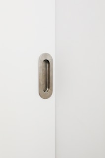 A minimalist image featuring a white door with a modern, oval-shaped inset metal handle.