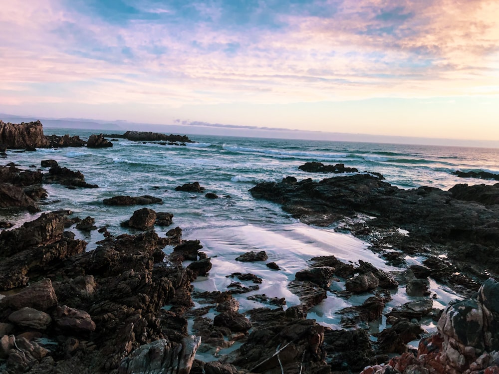 a rocky beach with a body of water and a sunset