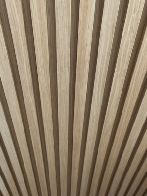Wooden panels are arranged in a vertical pattern, creating a repetitive and textured design. The wood has a natural beige and brown color, emphasizing the grain and texture.