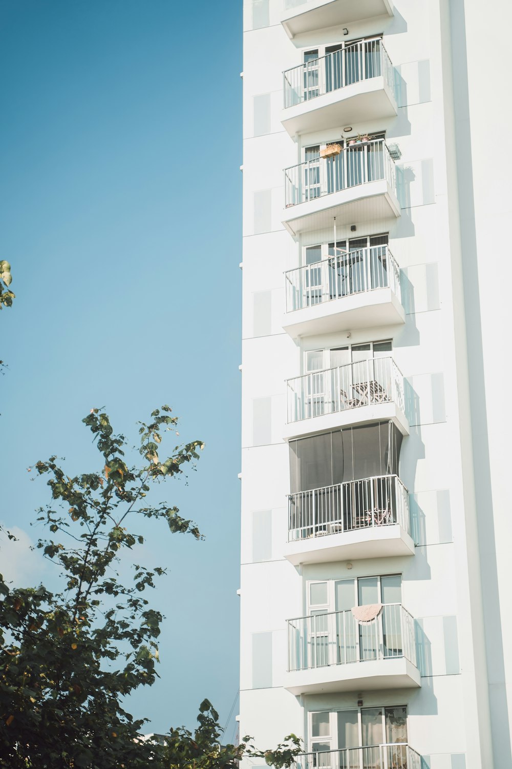 a tall white building with balconies and trees