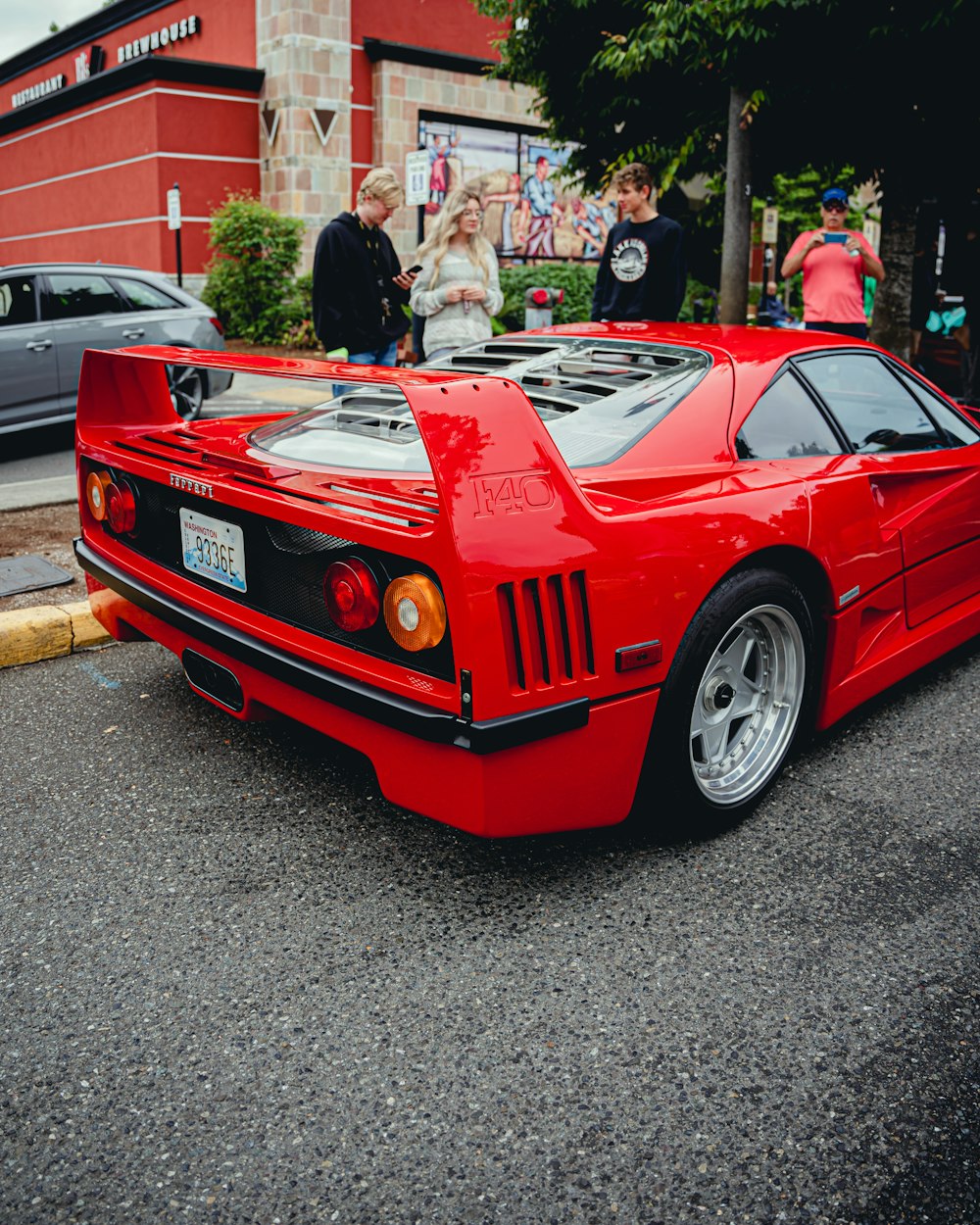 a red sports car parked on the side of a street with people standing around