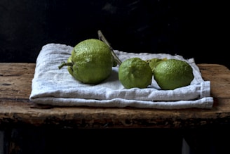 Fresh lime fruits arranged in a rustic basket with green leaves on wooden table.