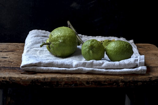 Fresh lime fruits arranged in a rustic basket with green leaves on wooden table.